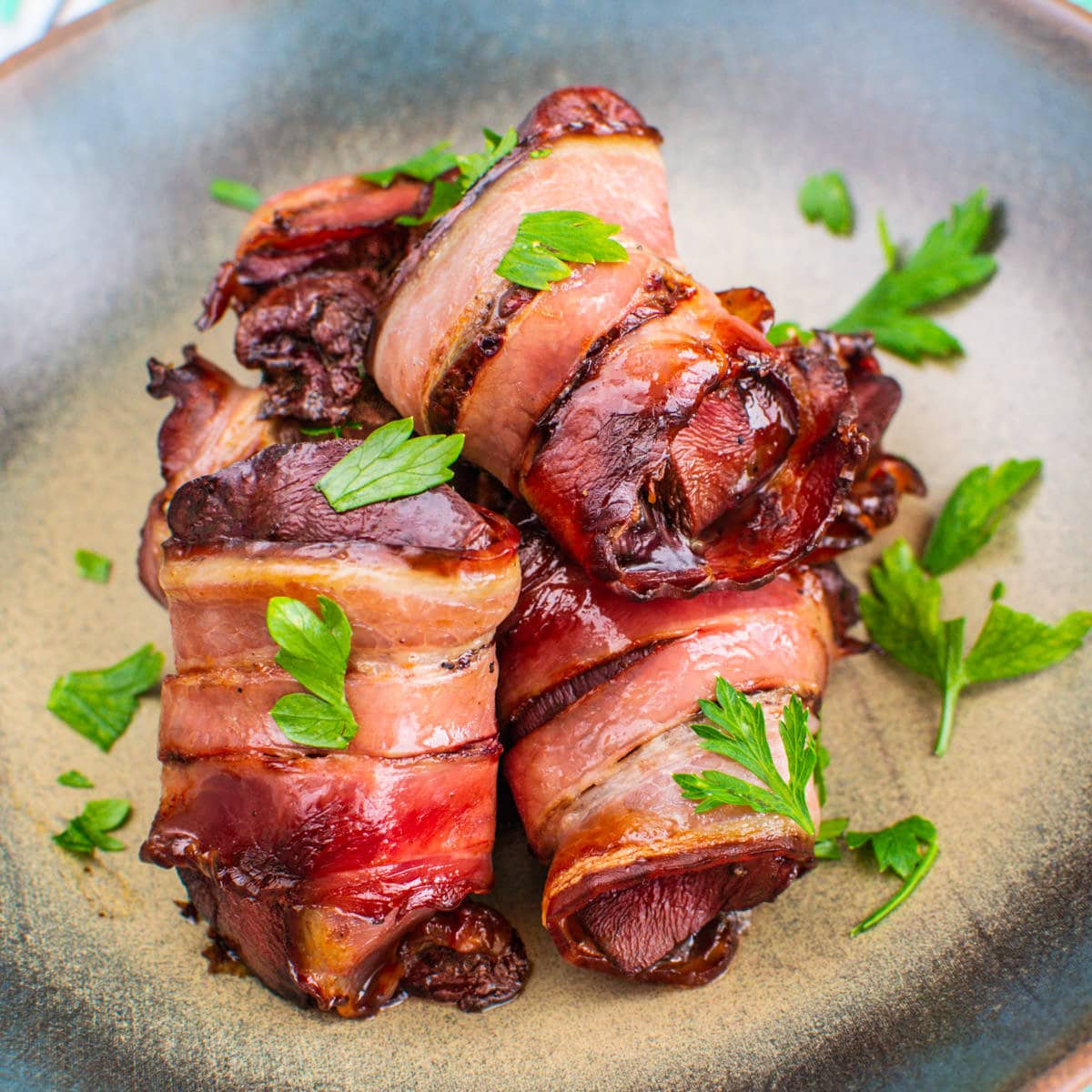 Close look of bacon wrapped turkey livers with copped parsley on a plate.