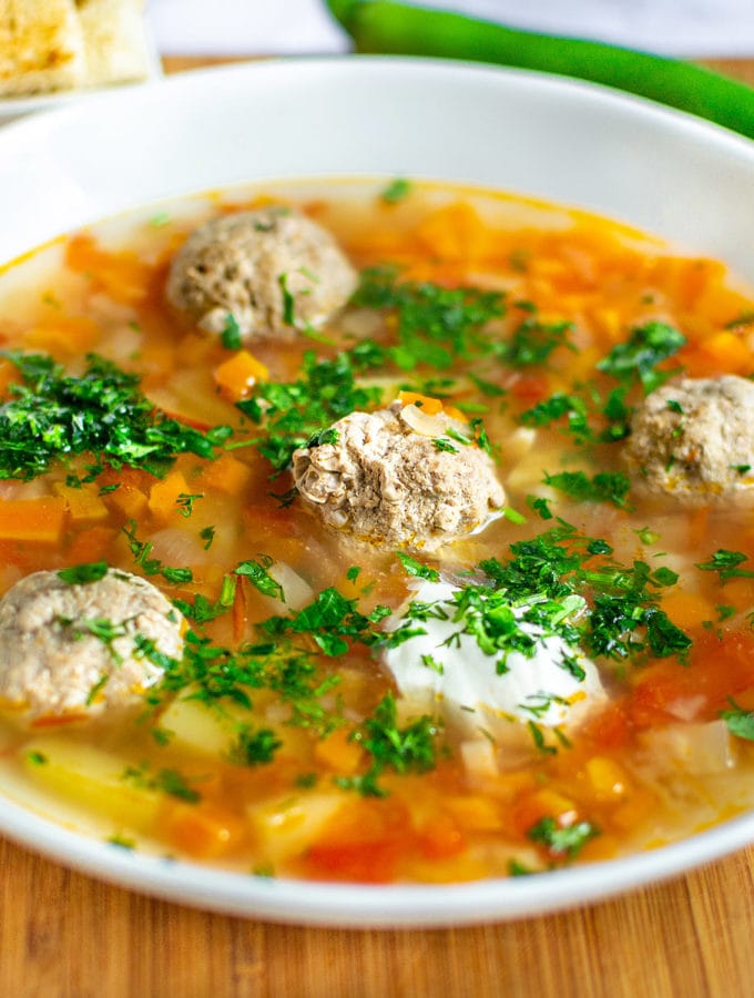 Soup with meatballs and vegetables in a white plate on a wooden cutting board.