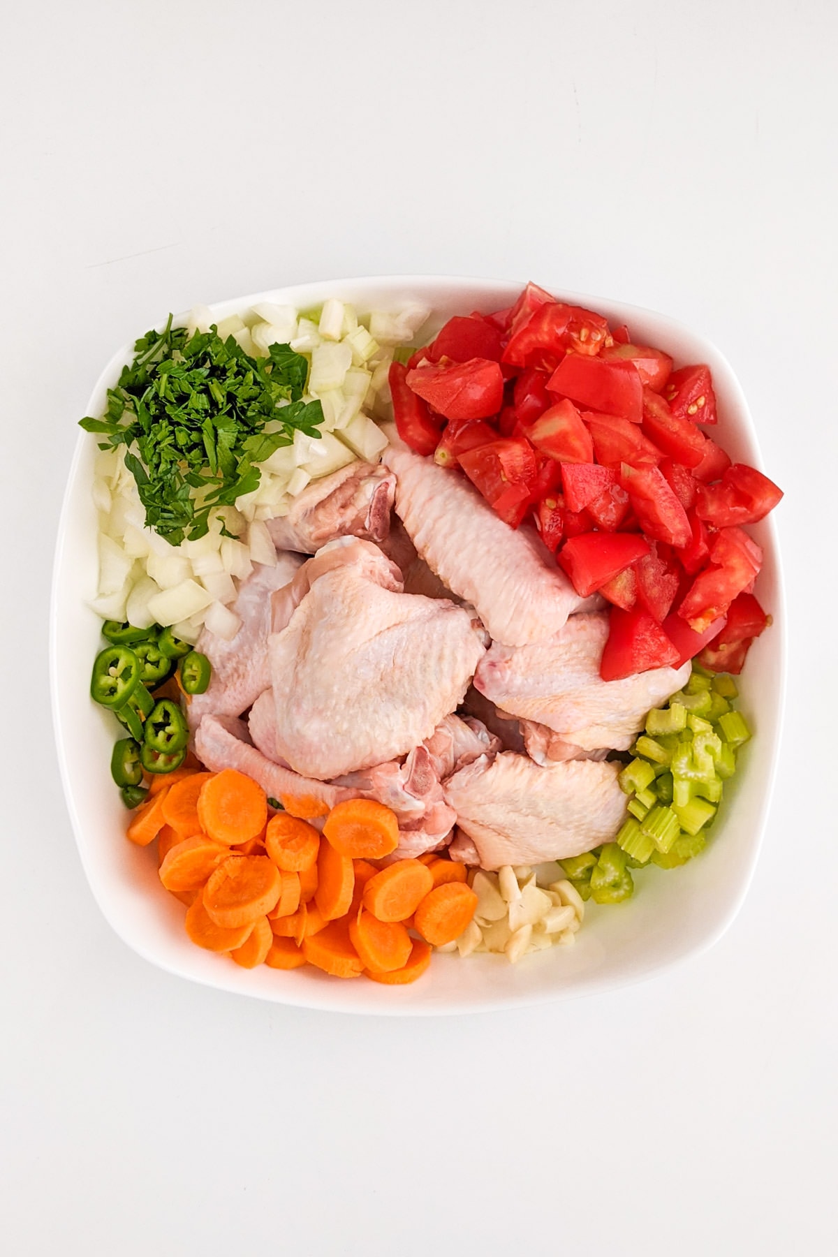 Chicken wings with chopped tomatoes, onions, parsley, carrots and celery in a white plate.