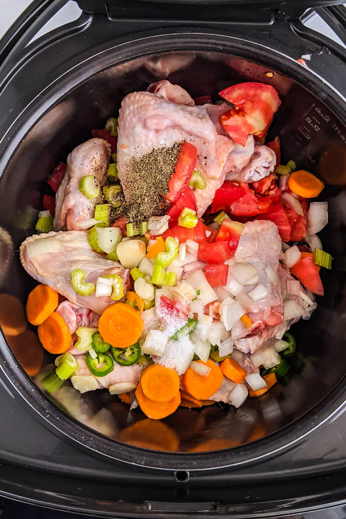 Slow cooker tray with chicken wings, with cubes of different vegetables and spices over them.