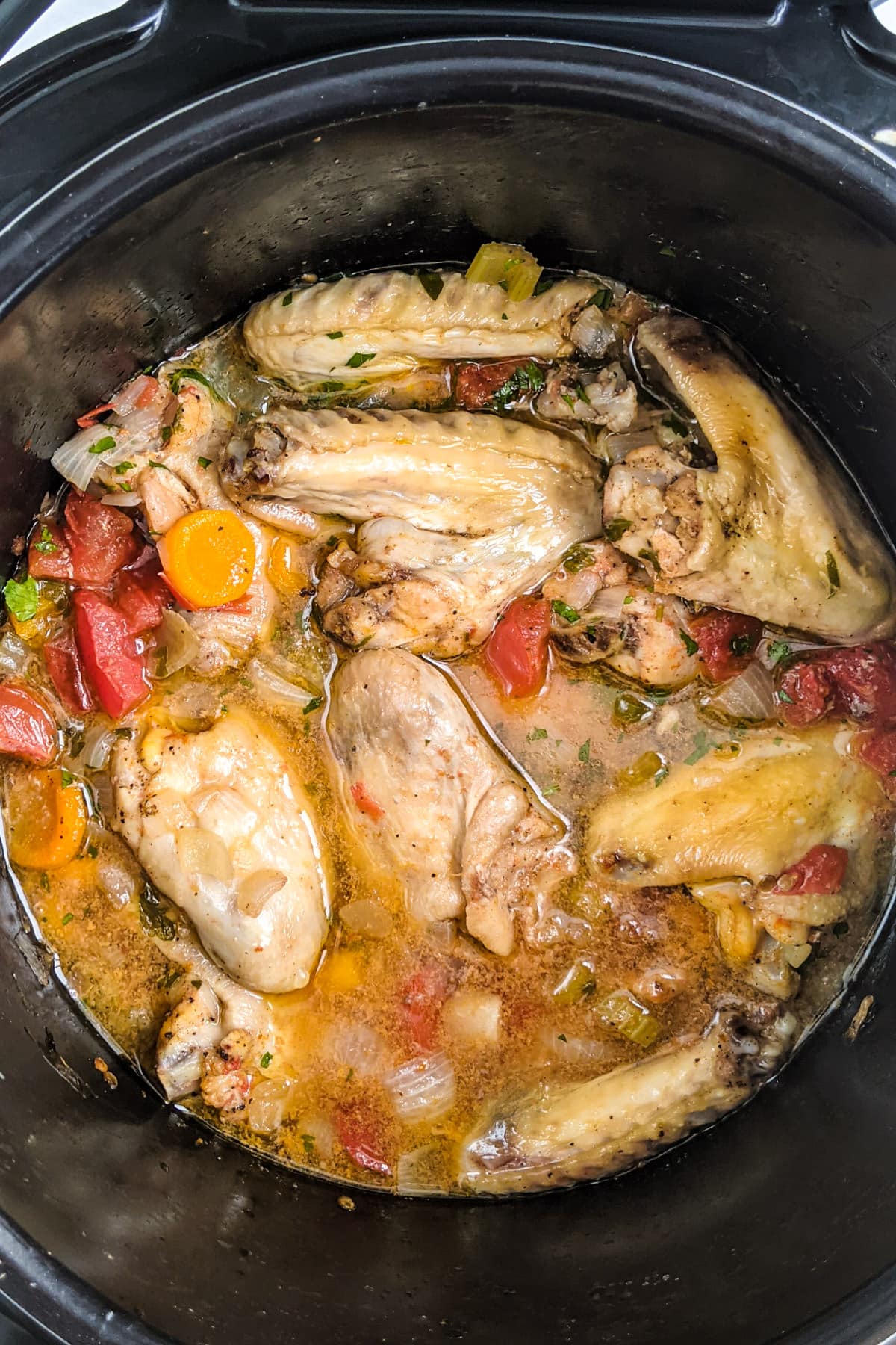 Simmered chicken wings with vegetables and juice in a slow cooker tray.