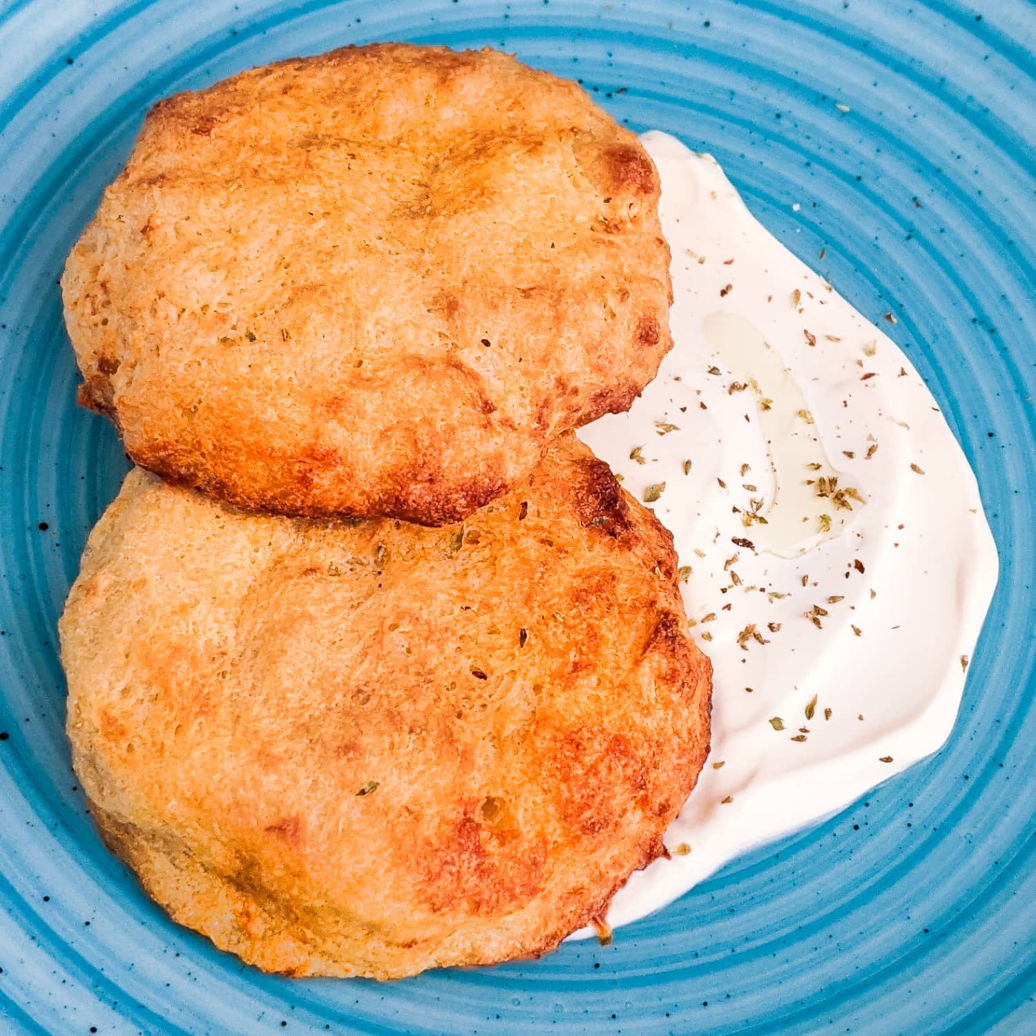 Close look of air fried hash brown patties with sour cream on a blue plate.
