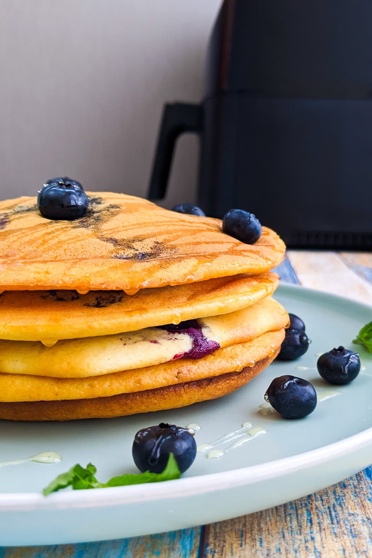 A plate of pancakes with blueberries and honey with air fryer in the background.