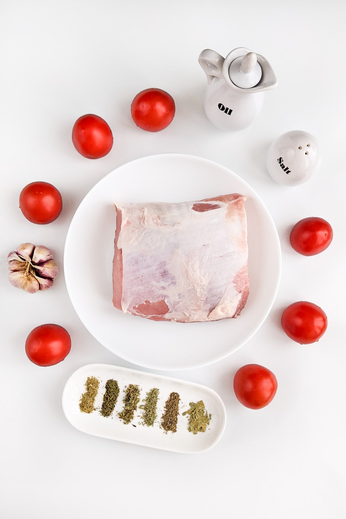 Pork loin with tomatoes, garlic and spices on white table.