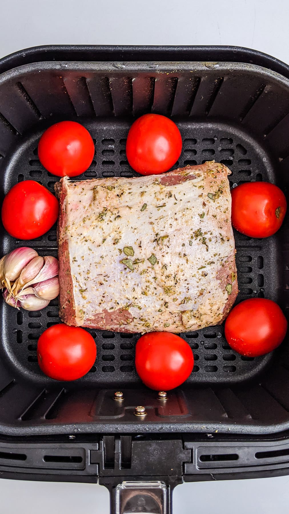 Seasoned Pork loin with tomatoes and garlic in air fryer basket.