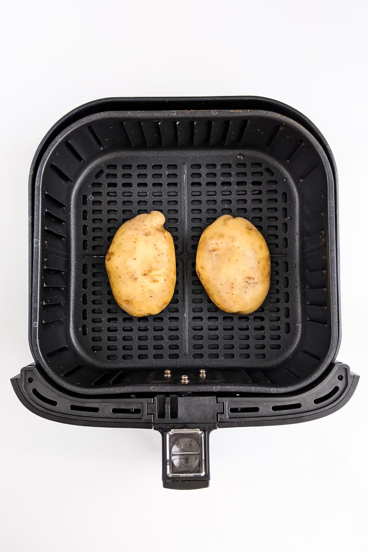 Top view of two potatoes in an air fryer basket.
