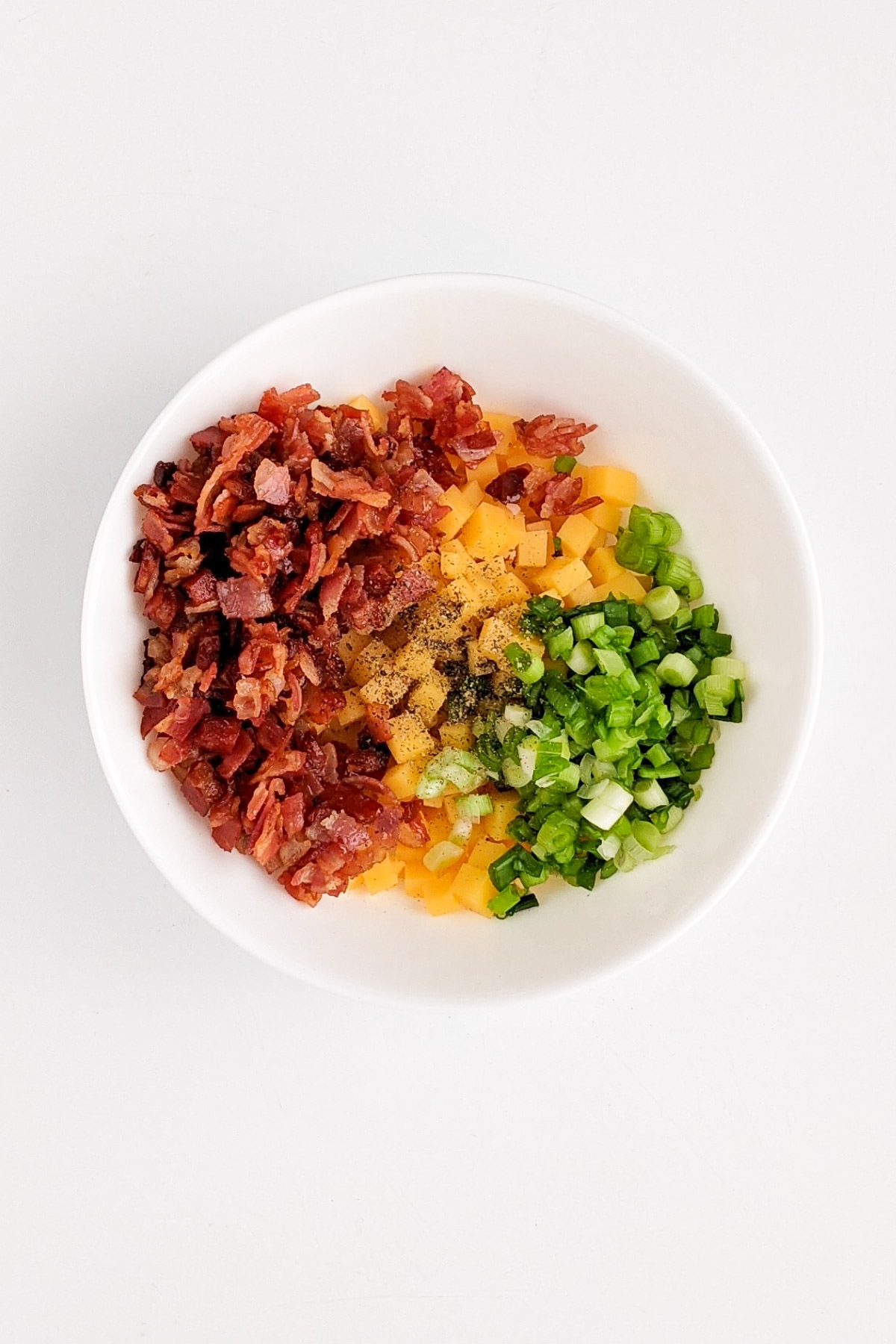 Cheddar cheese with bacon, green onions in a white plate.