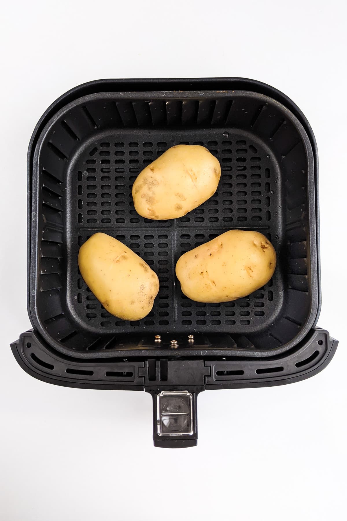 Top view of three potatoes in the air fryer basket.