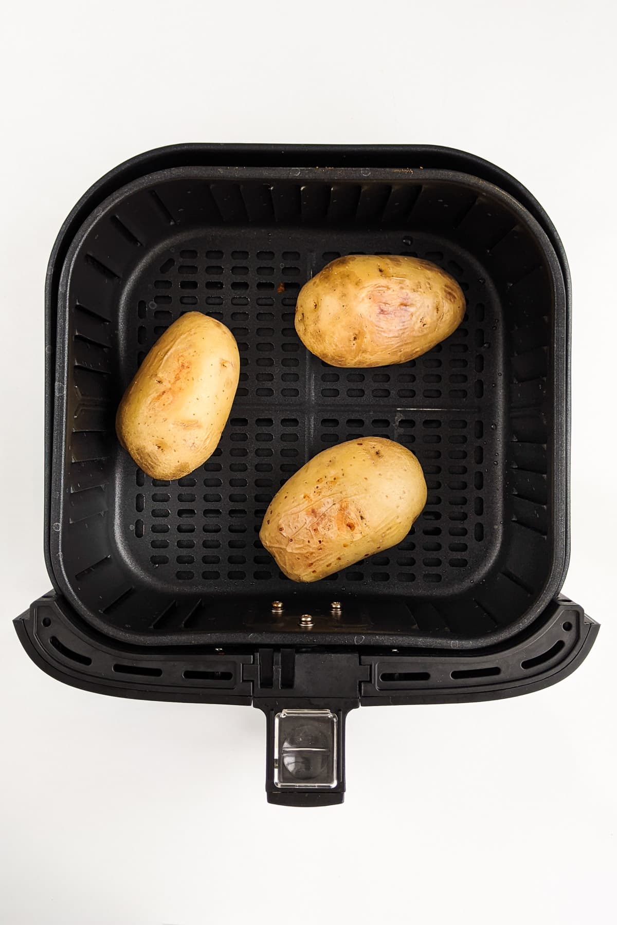 Top view of three baked potatoes in the air fryer basket.