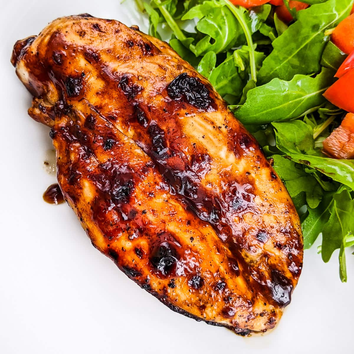 Close look at bbq chicken breast near salad leaves.