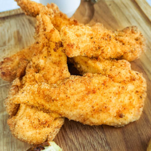 Wooden cutting board with chicken strips coated in bread crumbs.