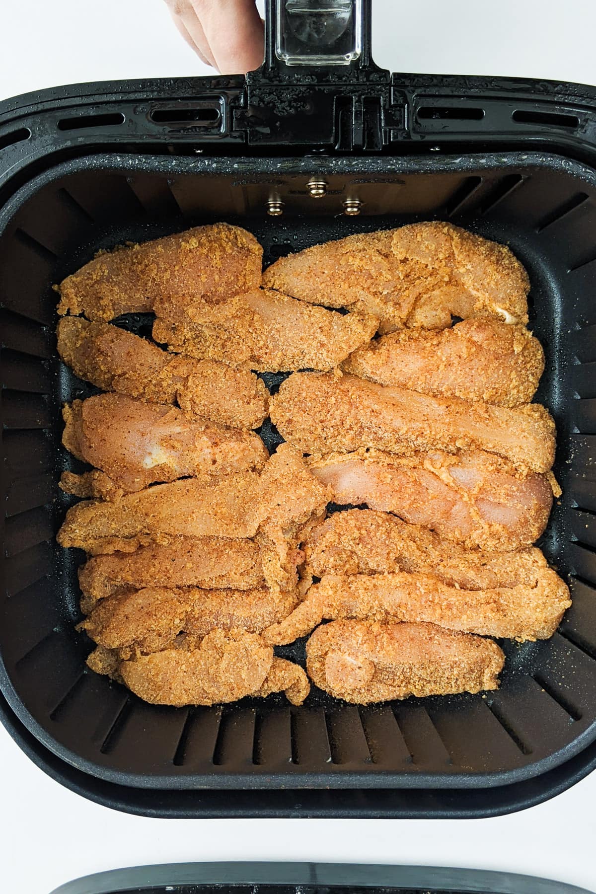 Chicken strips coated with bread crumbs in the air fryer basket.