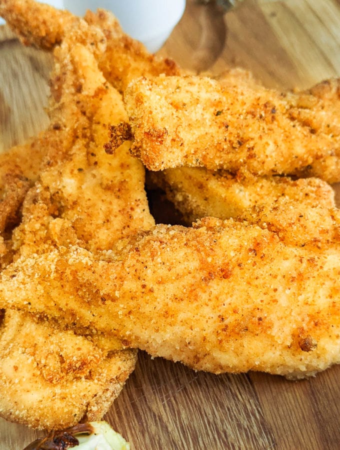 Wooden cutting board with chicken strips coated in bread crumbs.