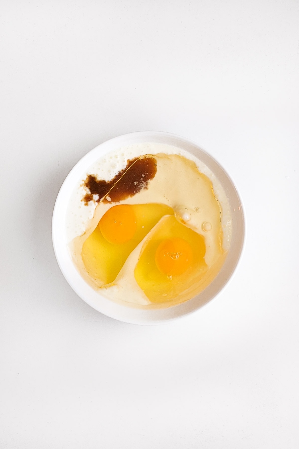 A plate with two raw eggs, buttermilk and vanilla extract.