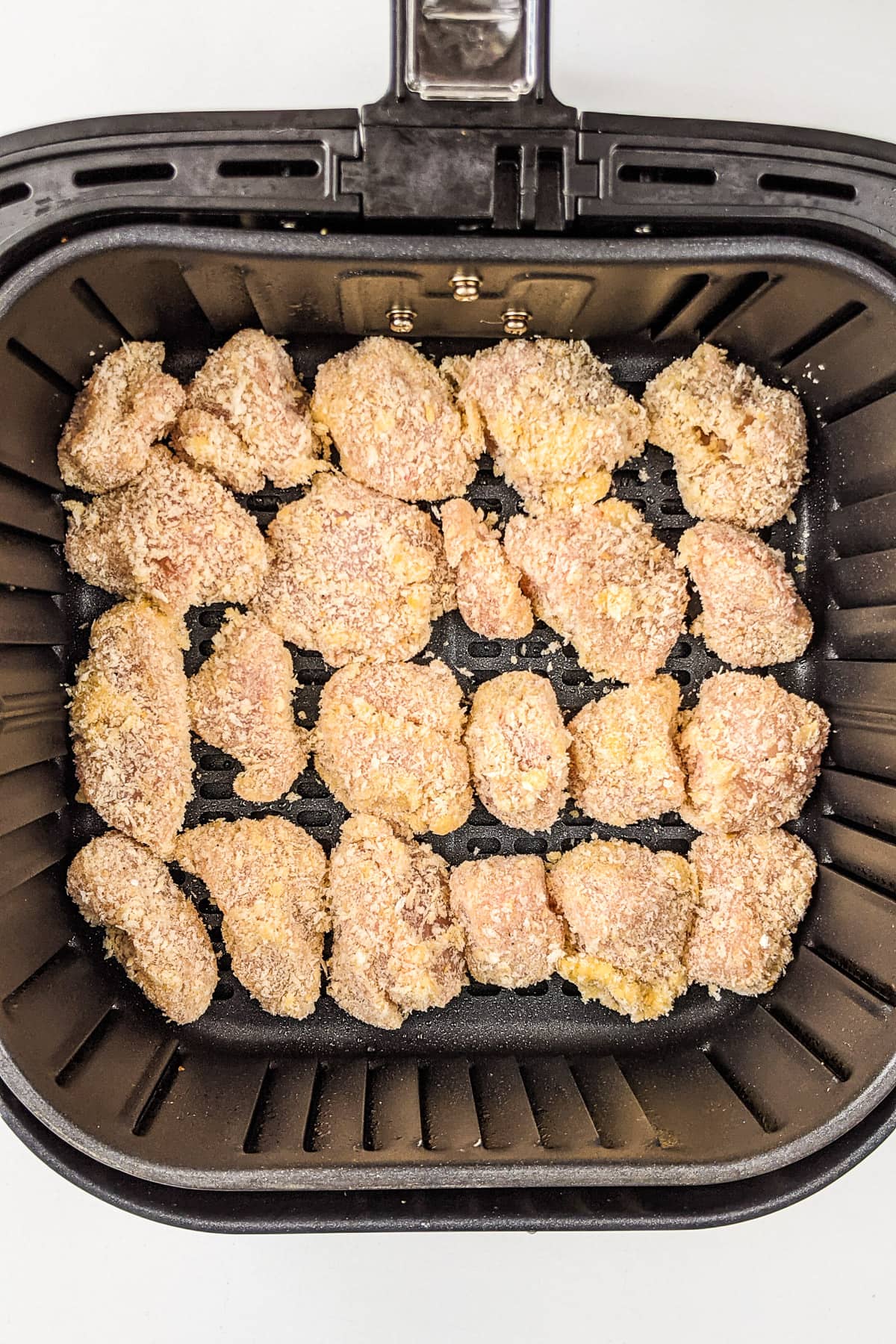 Air fryer basket with raw chicken nuggets in panko.