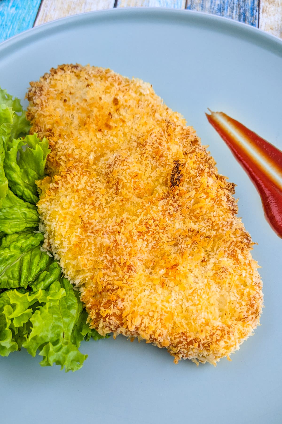 Chicken schnitzel coated in panko with tomato sauce and salad leaves.