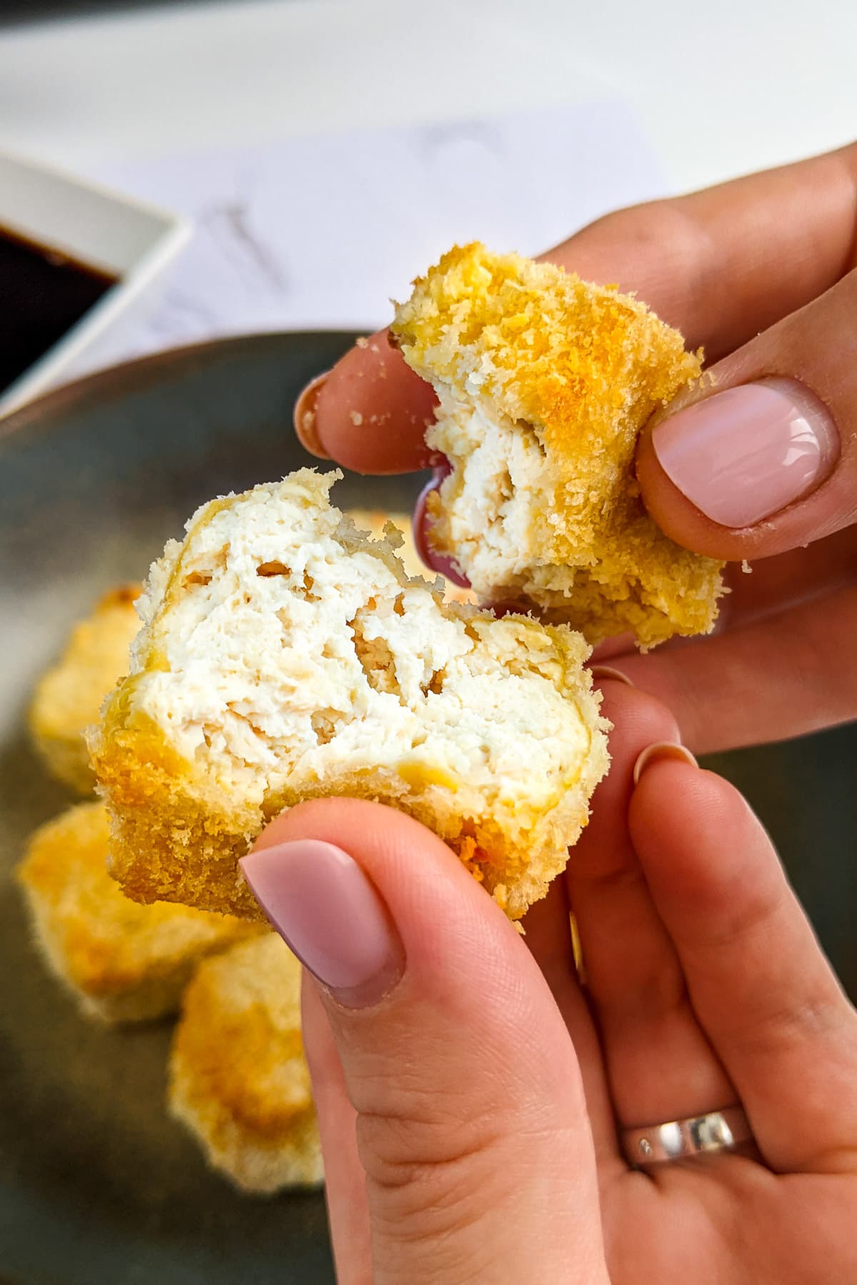 Two woman hands break one tofu nuggets to see the inner texture.