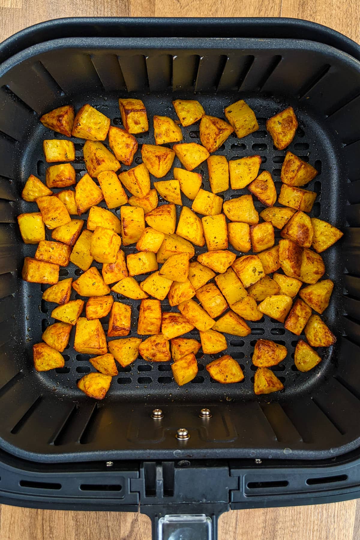 Top view of roasted diced potatoes in an air fryer basket.