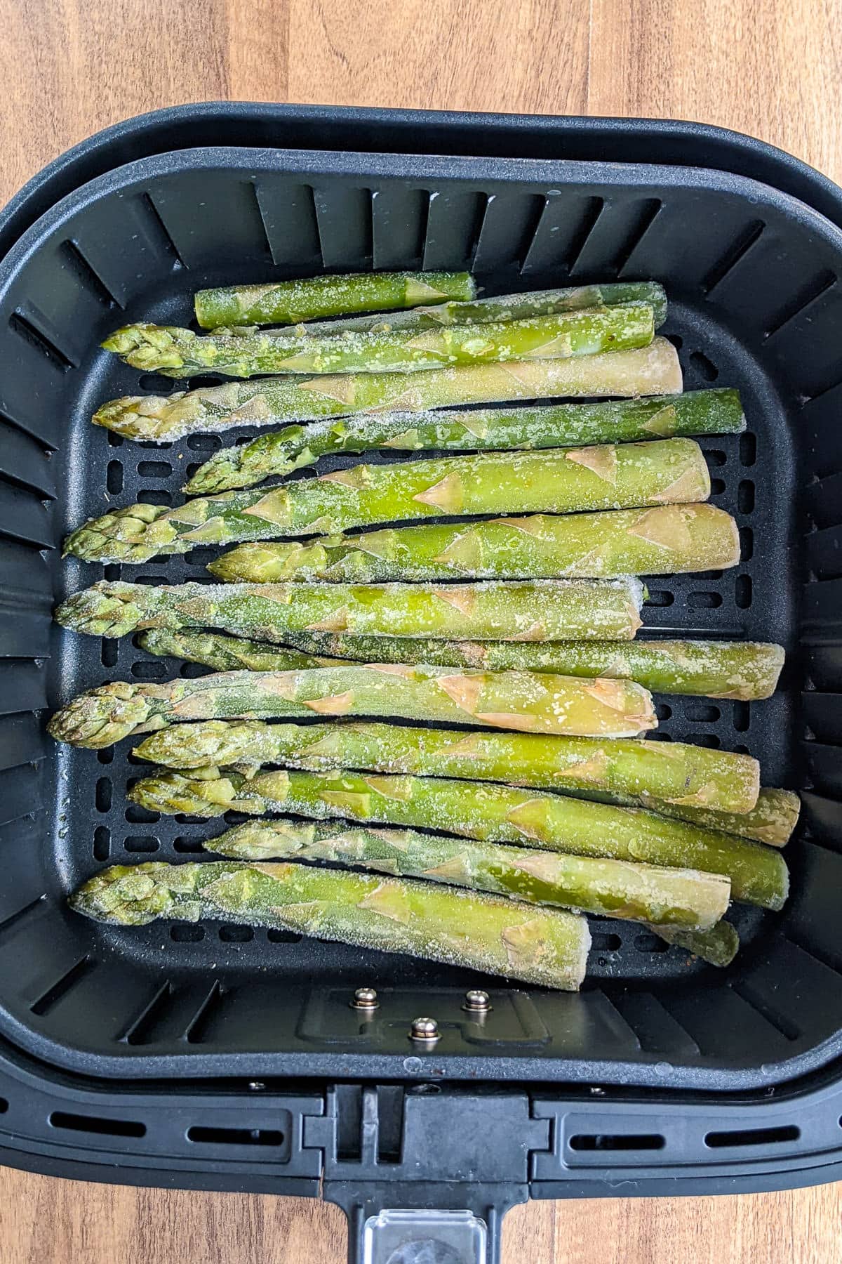 Top view of air fryer basket full with frozen asparagus.