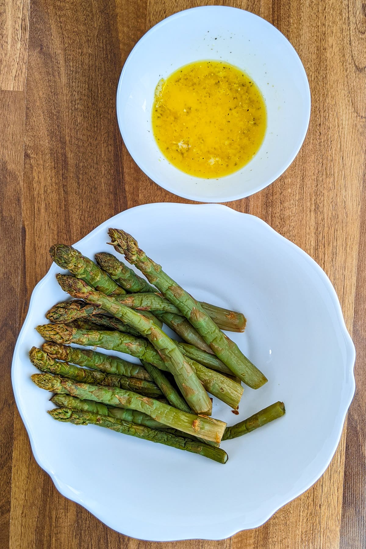 Plate with cooked asparagus near a plate with marinade.