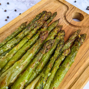Close look of air fried asparagus on a wooden cutting board.
