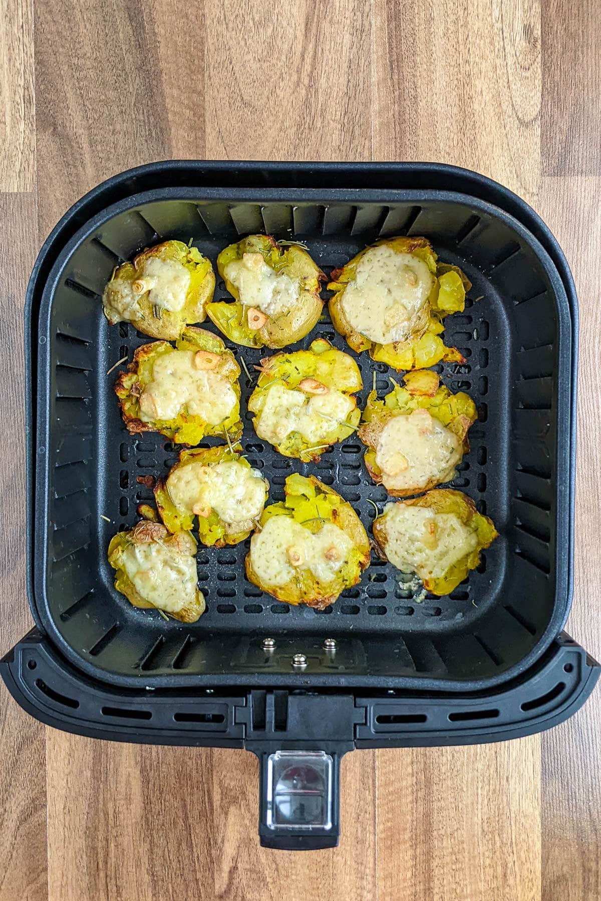 Top view of air fryer basket with roasted smashed potatoes with cheese, garlic and rosemary.