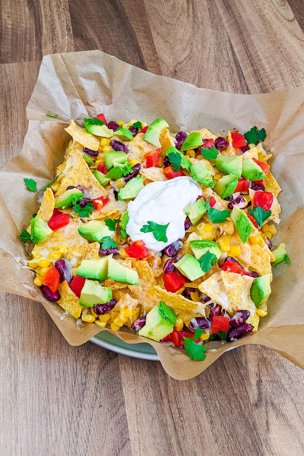 A plate with parchment paper with air fryer nachos with sour cream and chopped parsley.