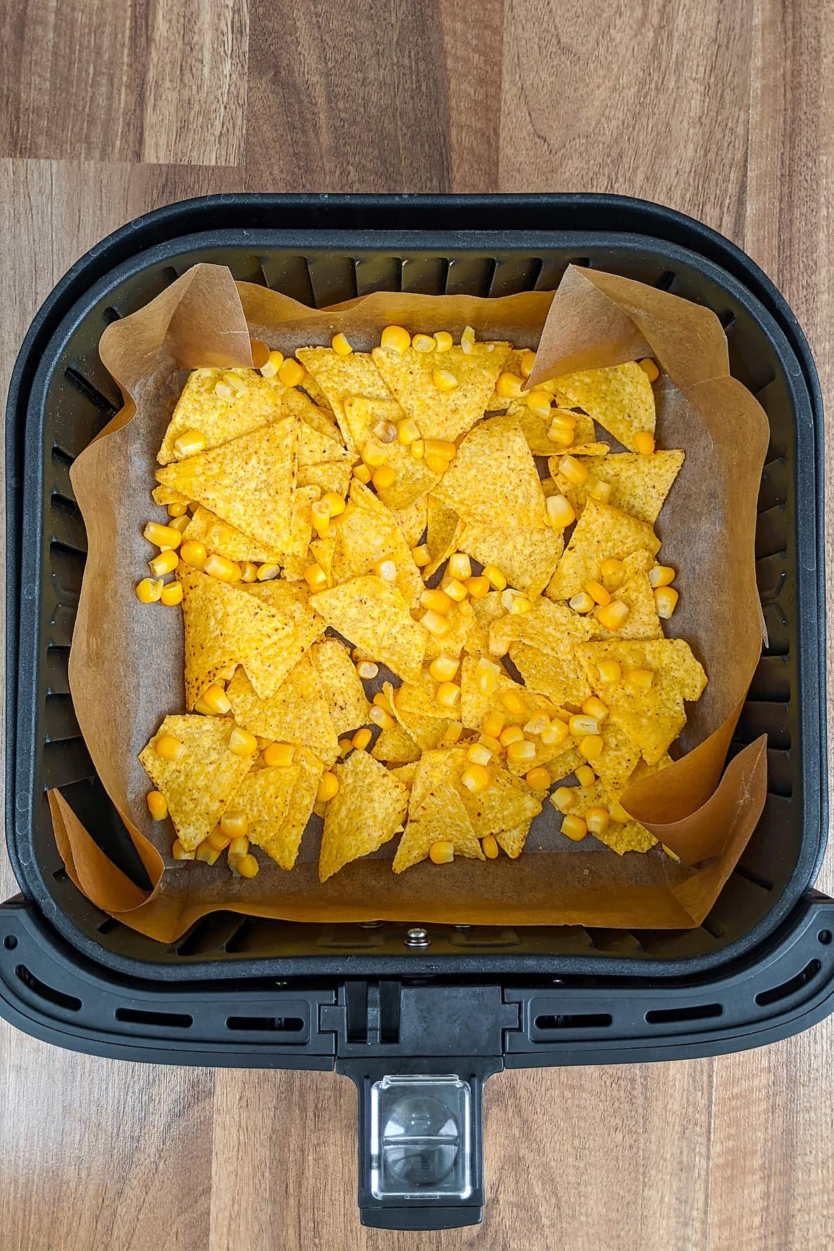 Air fryer basket with tortilla chips and canned corn.