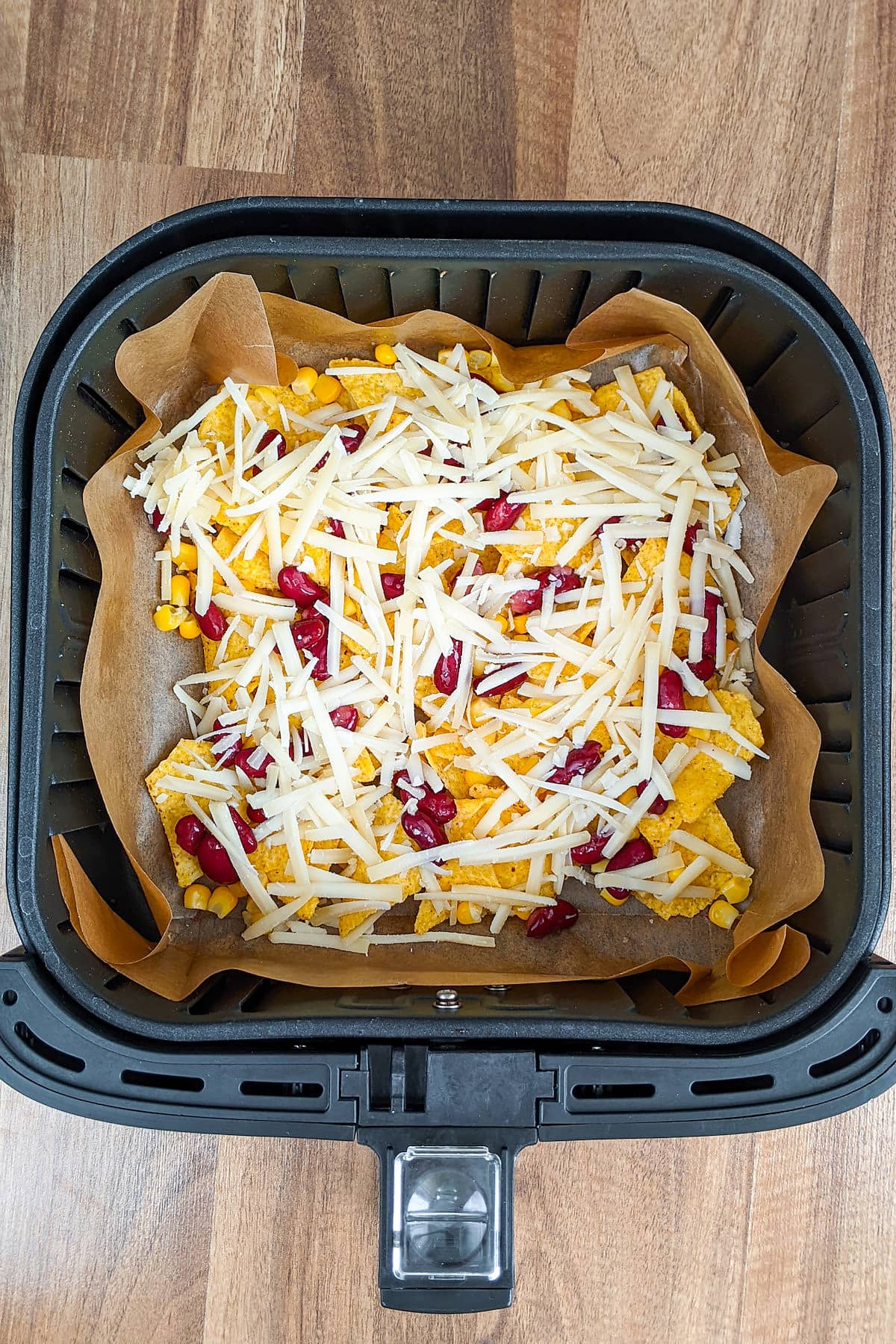 Air fryer basket with tortilla chips with shredded gruyere cheese, tortillas and beans.