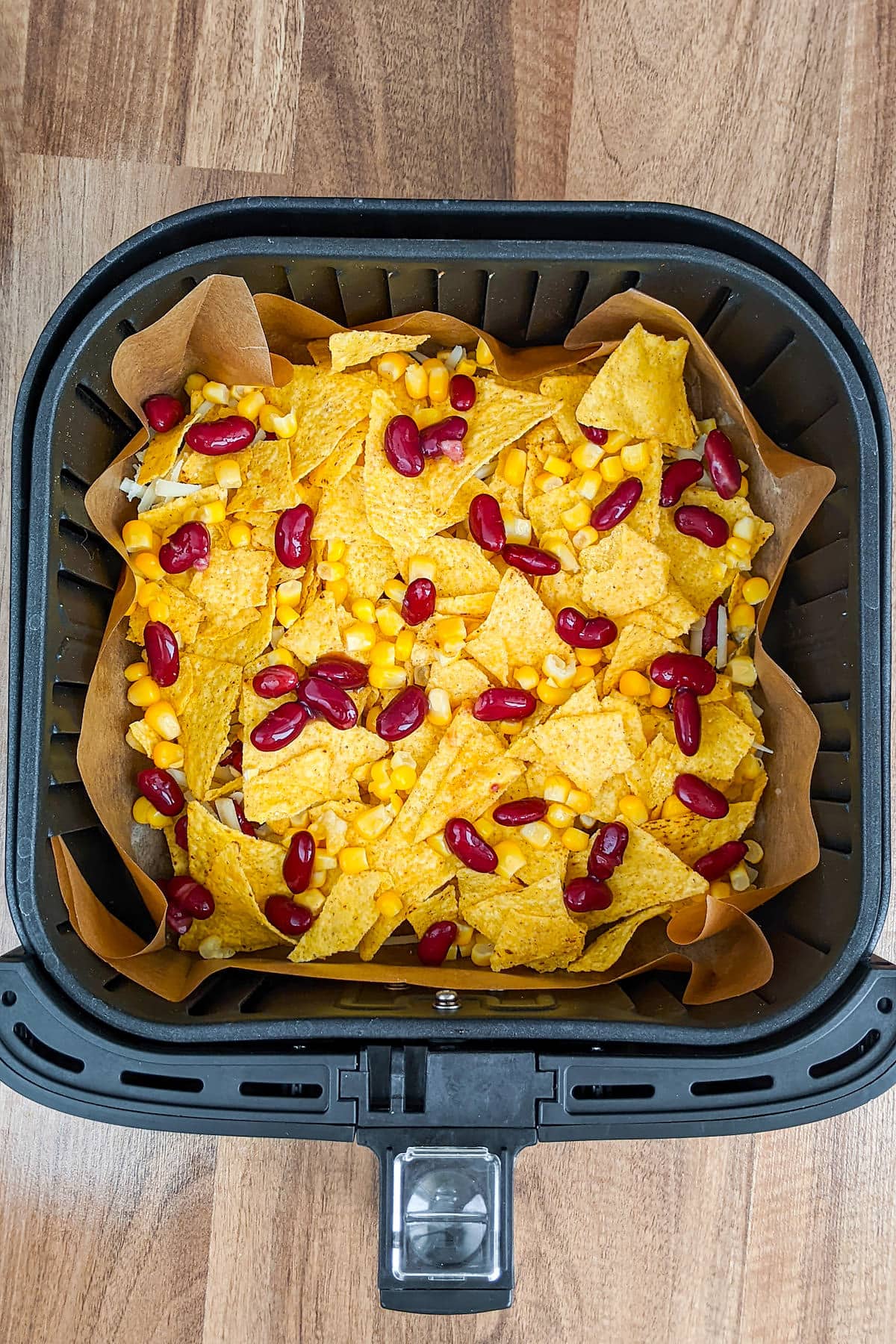 Air fryer basket with tortilla chips with canned corn and black beans.