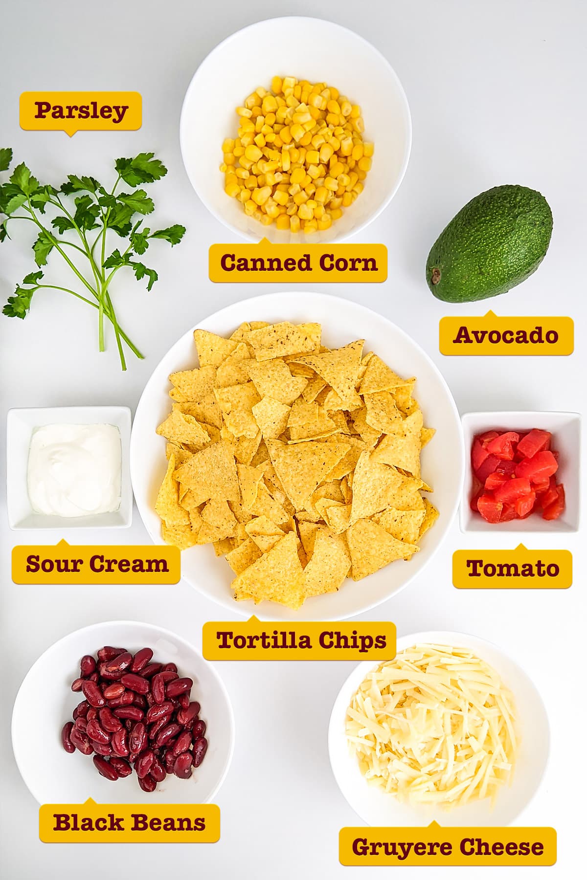 Tortilla chips with cheese, tomatoes, canned black beans, avocado, and corn on a white table.