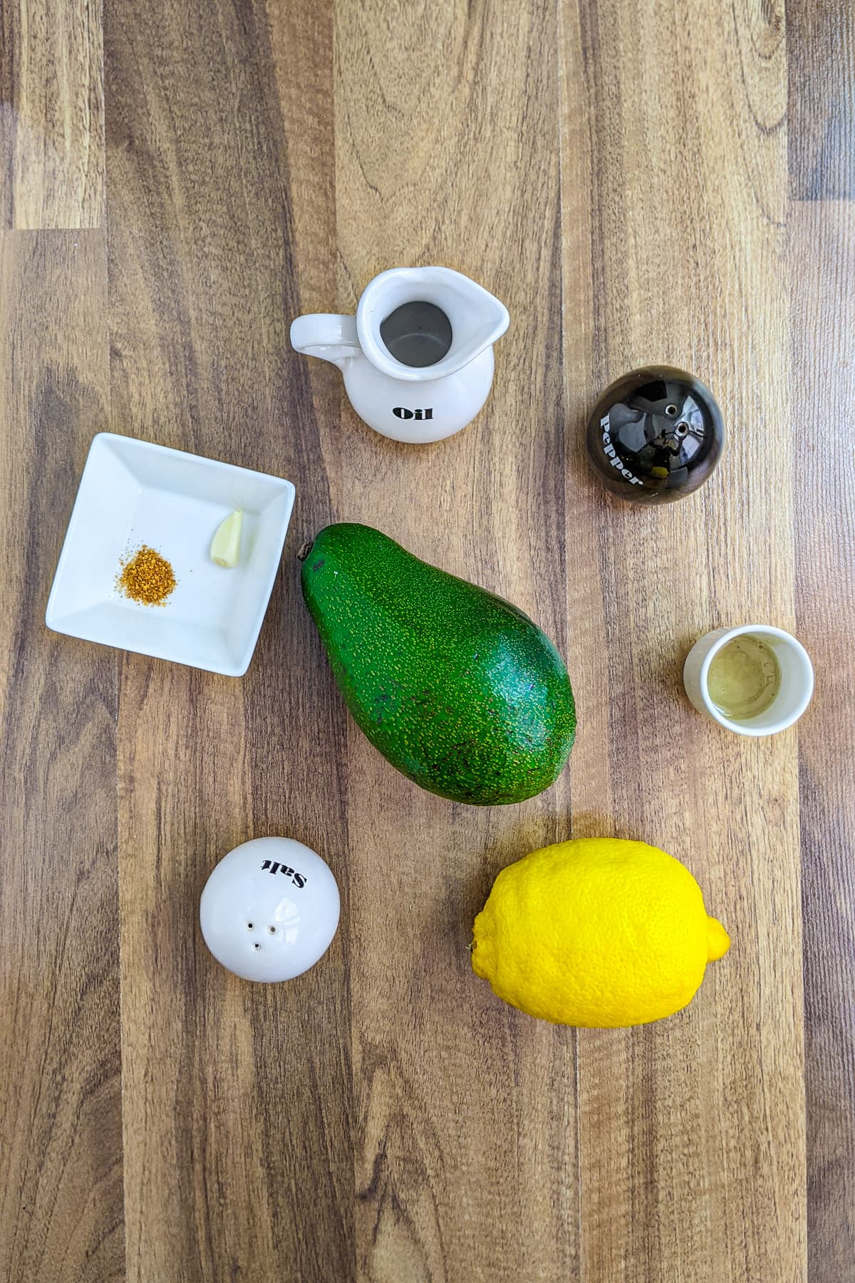 Top view of avocado, lemon, garlic and seasonings on a white table.