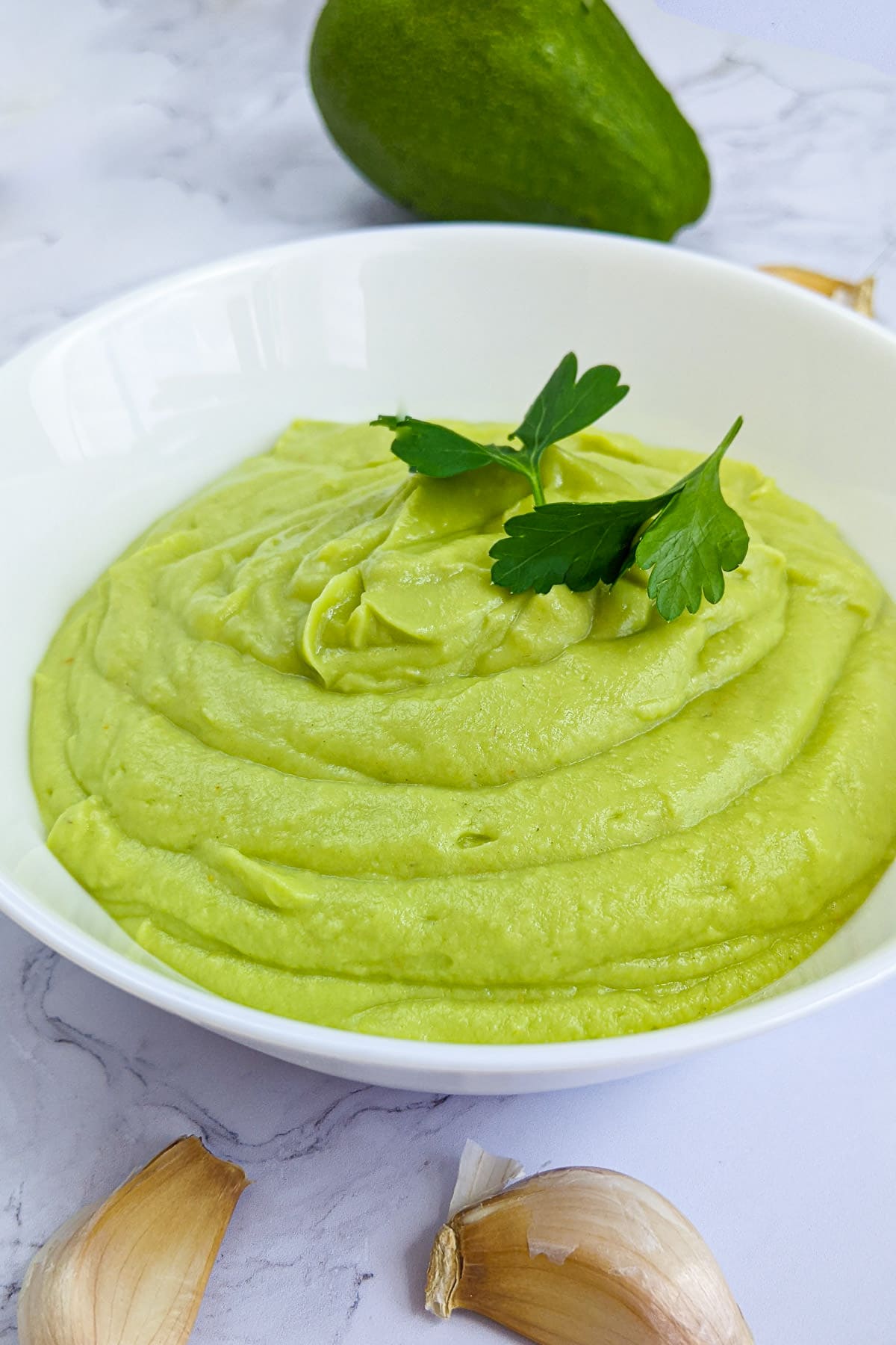 White plate with creamy avocado sauce with parsley, and garlic.