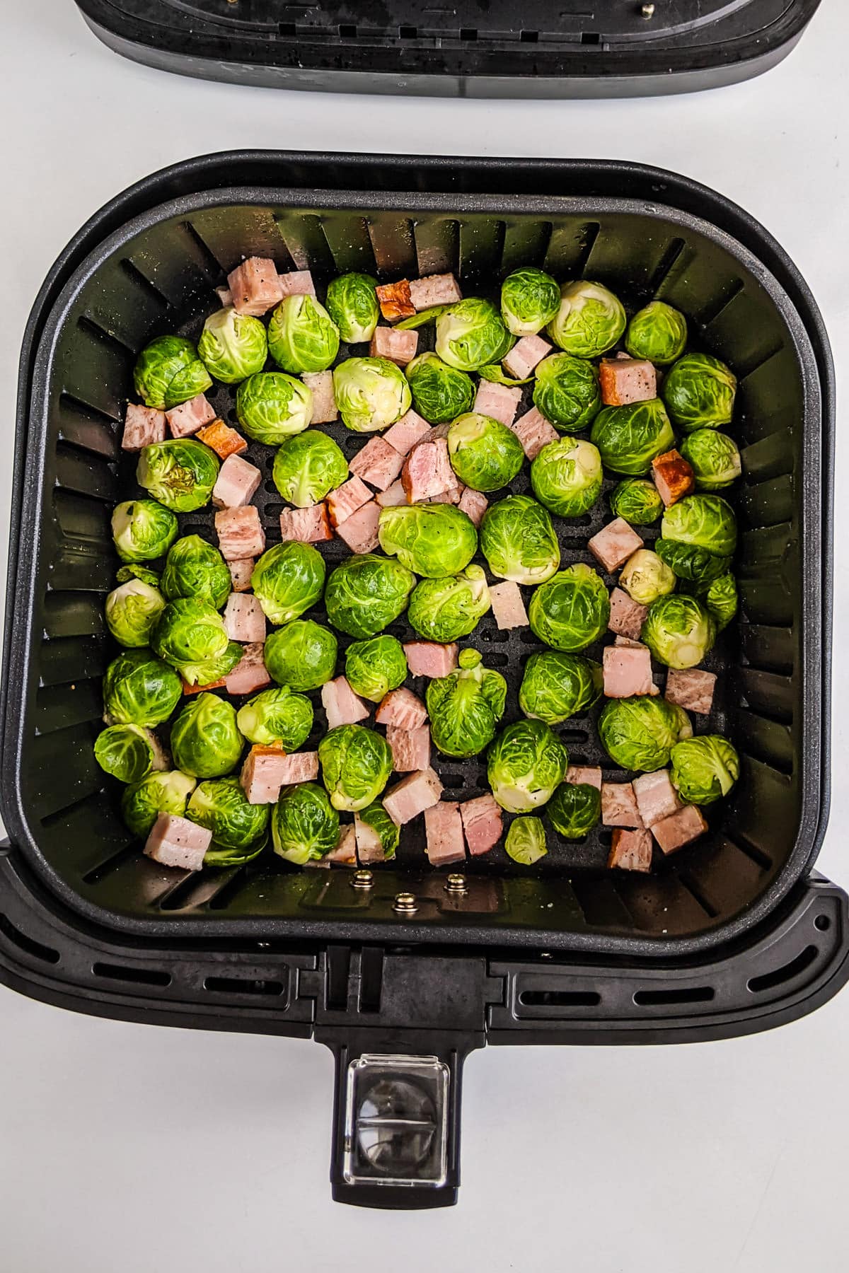 Top view of air fryer basket with brussels sprouts with bacon.