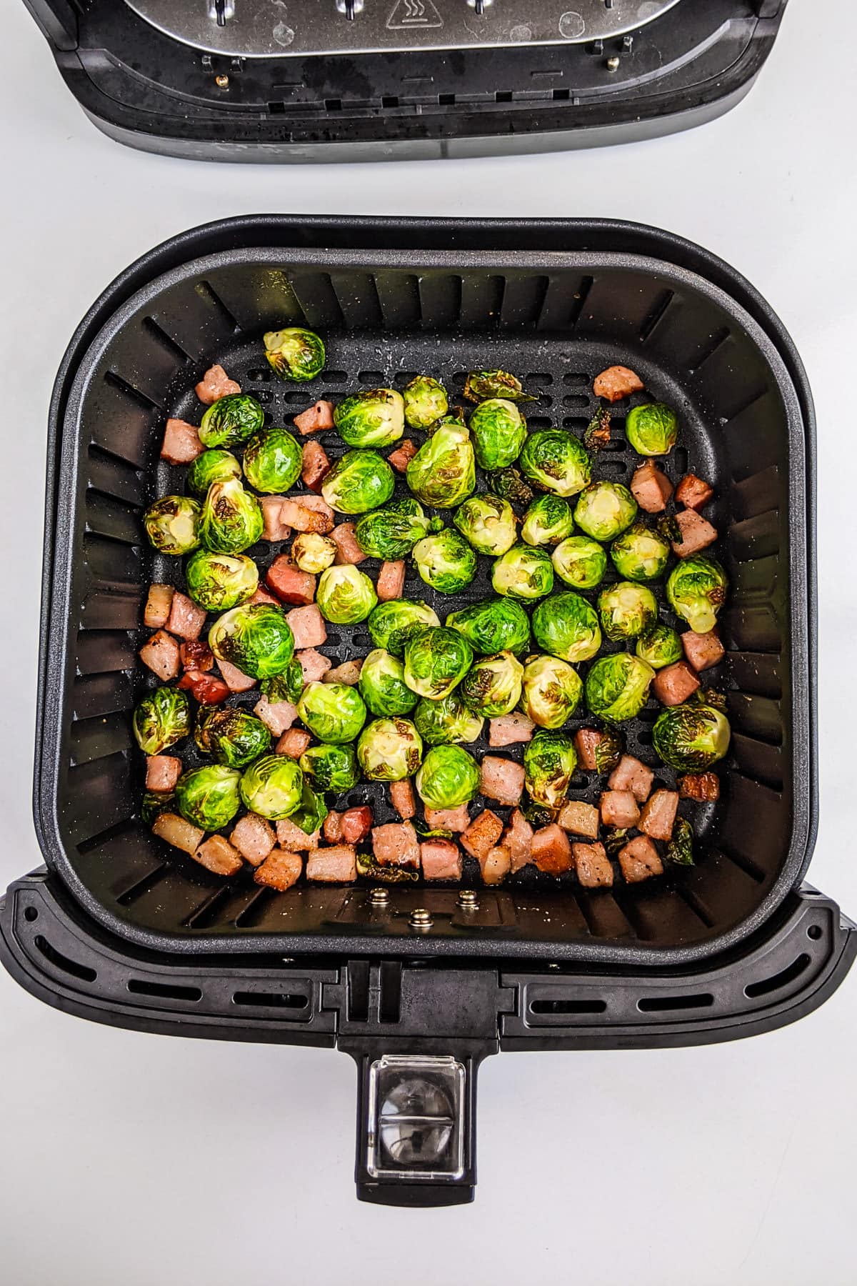 Top view of air fryer basket with brussels sprouts with bacon.