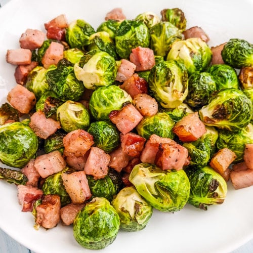 Brussels sprouts with bacon on a white plate.