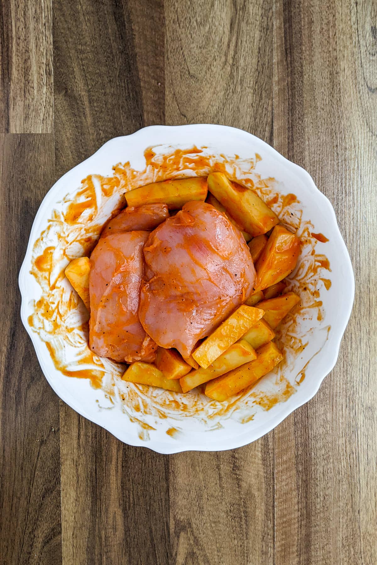 White plate with chicken breast and potatoes marinating in a buffalo sauce.