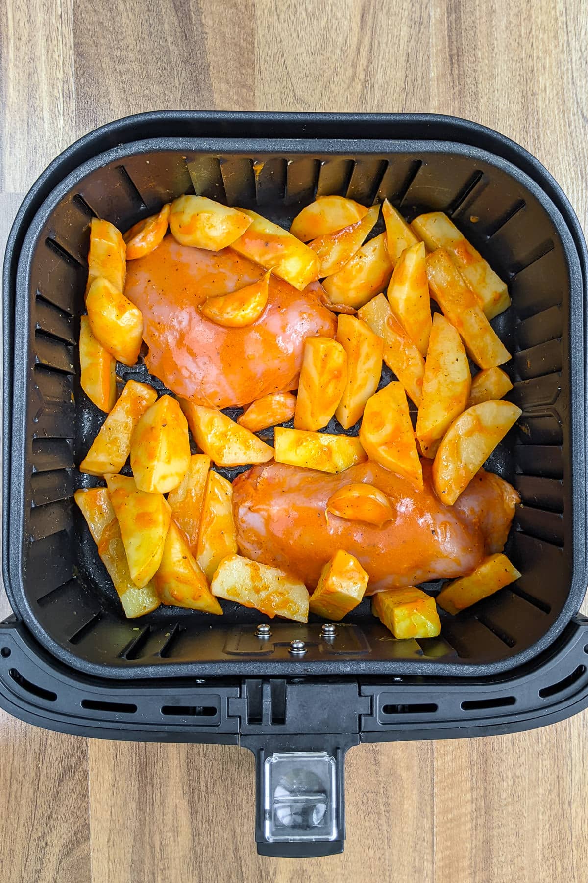 Chicken breasts and potatoes in air fryer marinated in buffalo sauce.