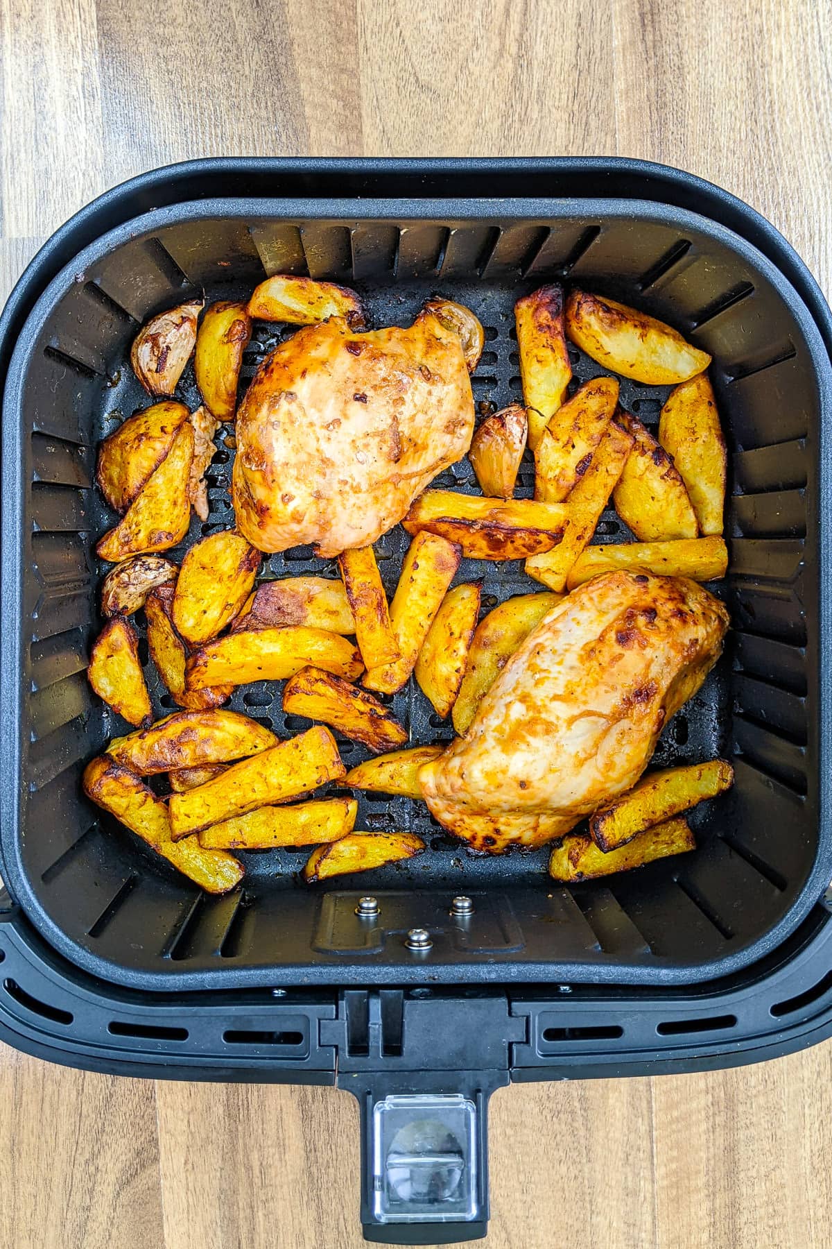 Air fryer basket with chicken breast and potatoes.