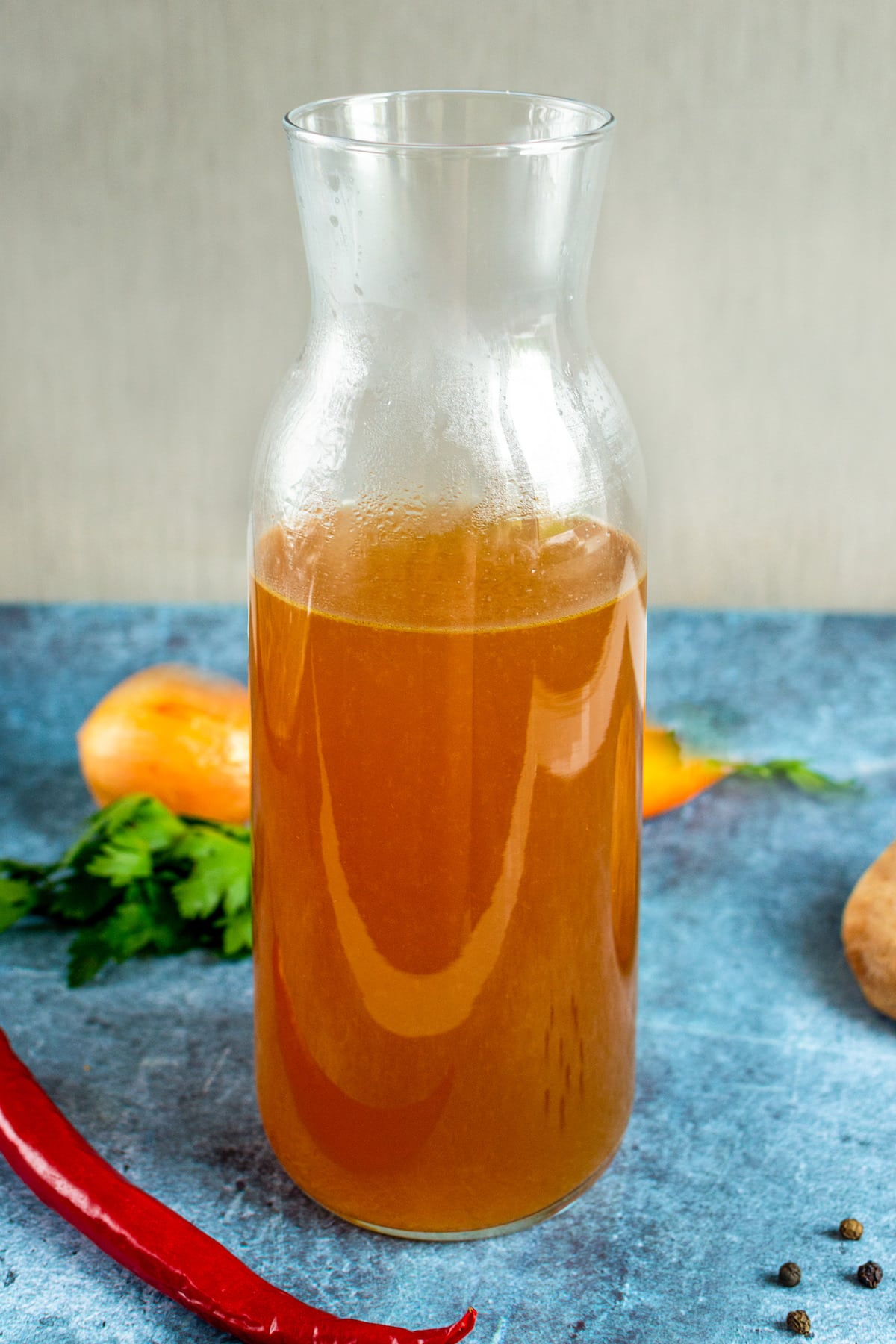 transparent bottle with vegetable broth on a blue table.