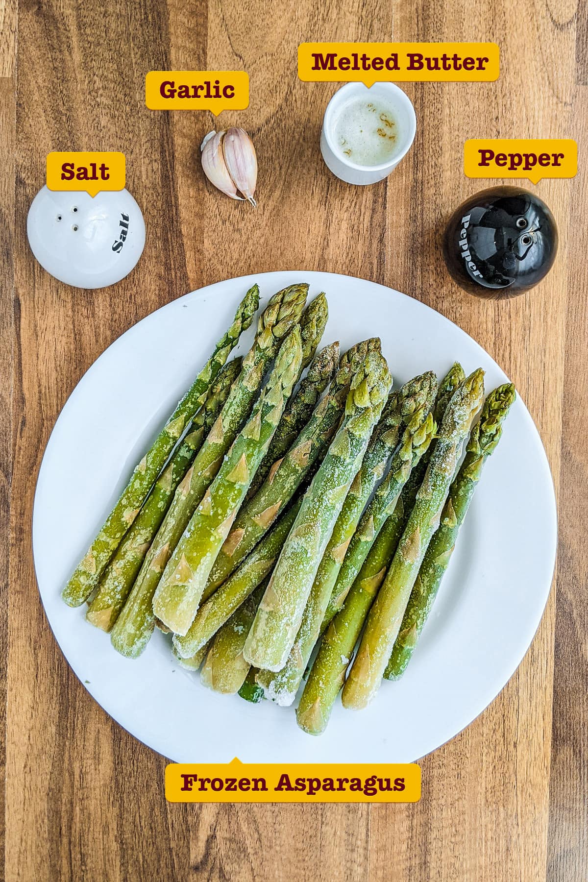 Frozen asparagus with garlic, melted butter, salt and pepper on a wooden table.