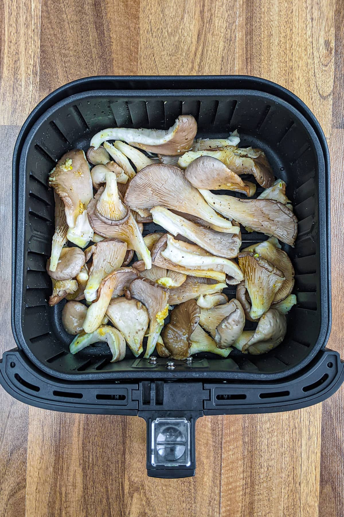 Air fryer basket with marinated oyster mushrooms.
