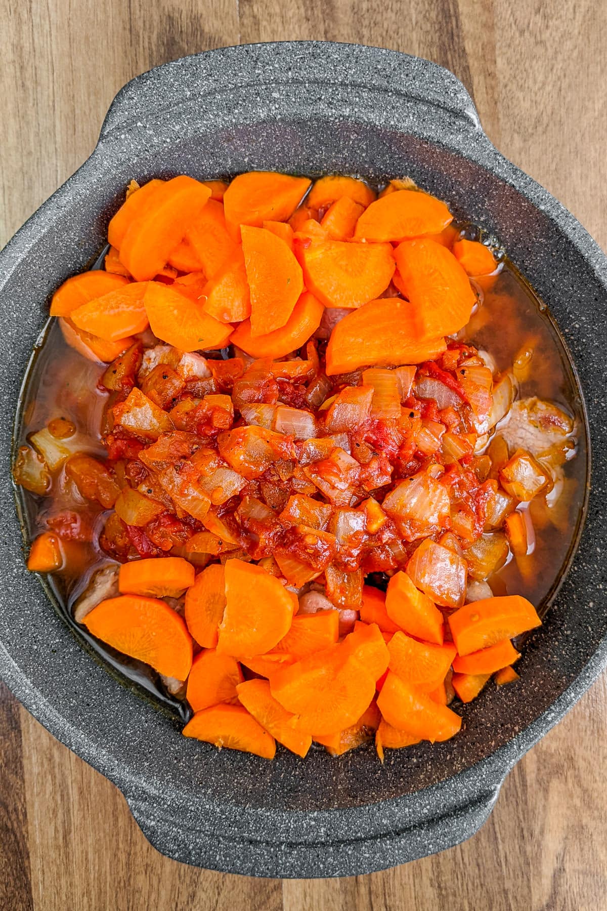 Pork stew with sliced carrots in a sauce pan.