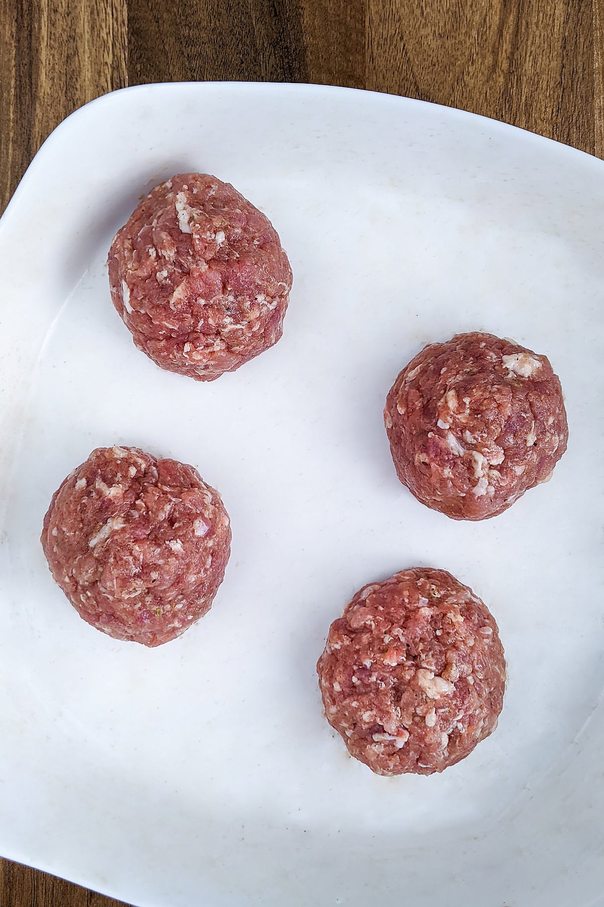 Four balls with ground pork meat in a white plate.
