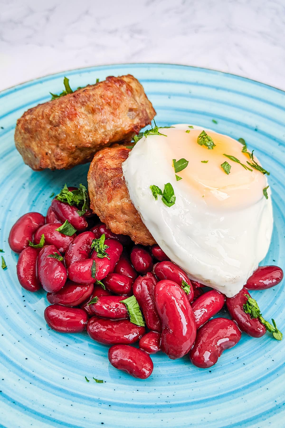 Blue plate with homemade air fryer sausages, canned beans and fried egg.