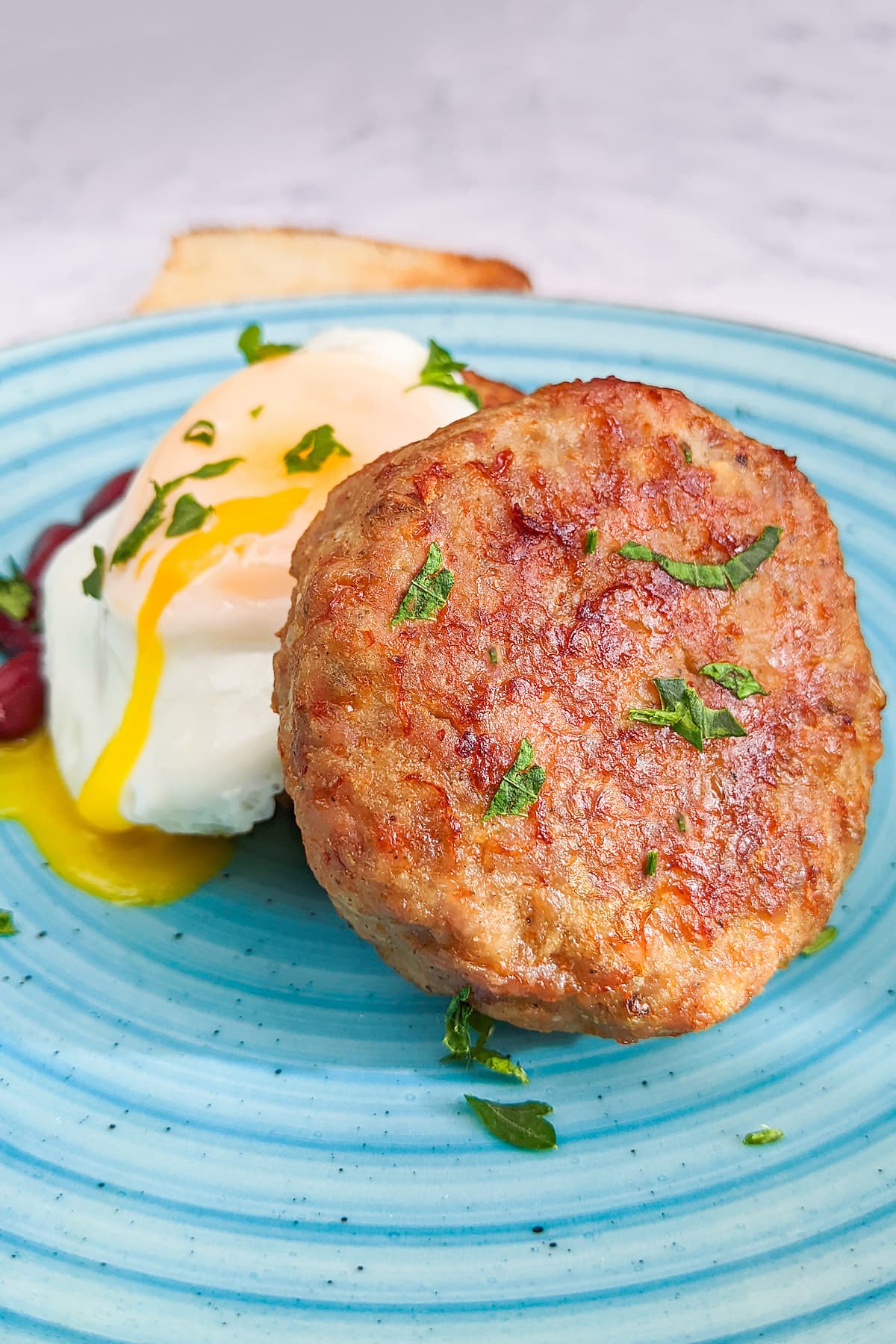 Air fried sausage patties with fried egg and chopped parsley on a blue plate.