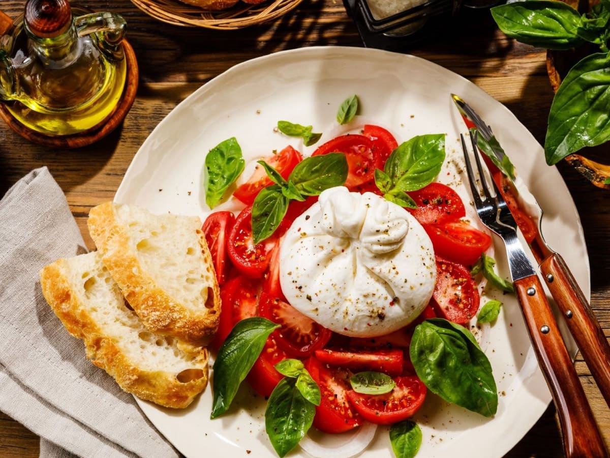 Top view of burrata with basil leaves, tomatoes and two slices of bruschetti.