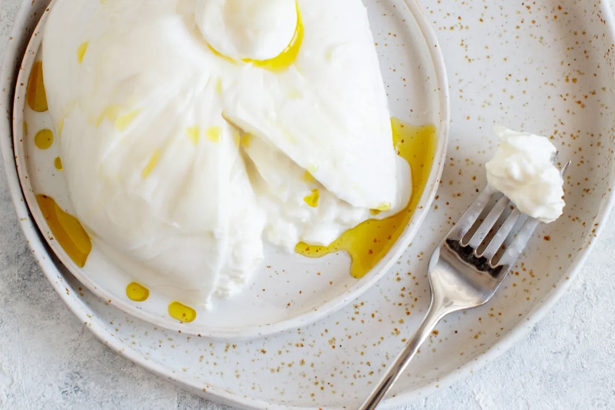 Top view of two plates with sliced burrata and a fork near.