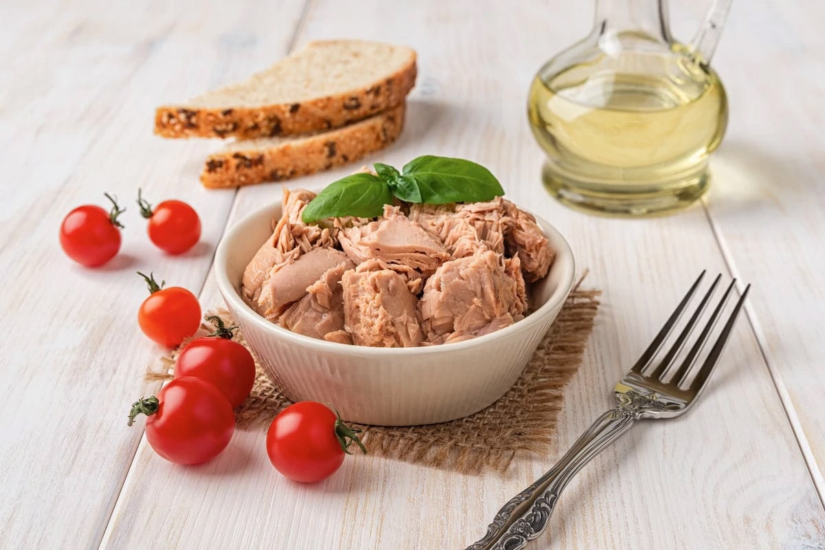 White plate with canned tuna, fork, cherry tomatoes and olive oil.