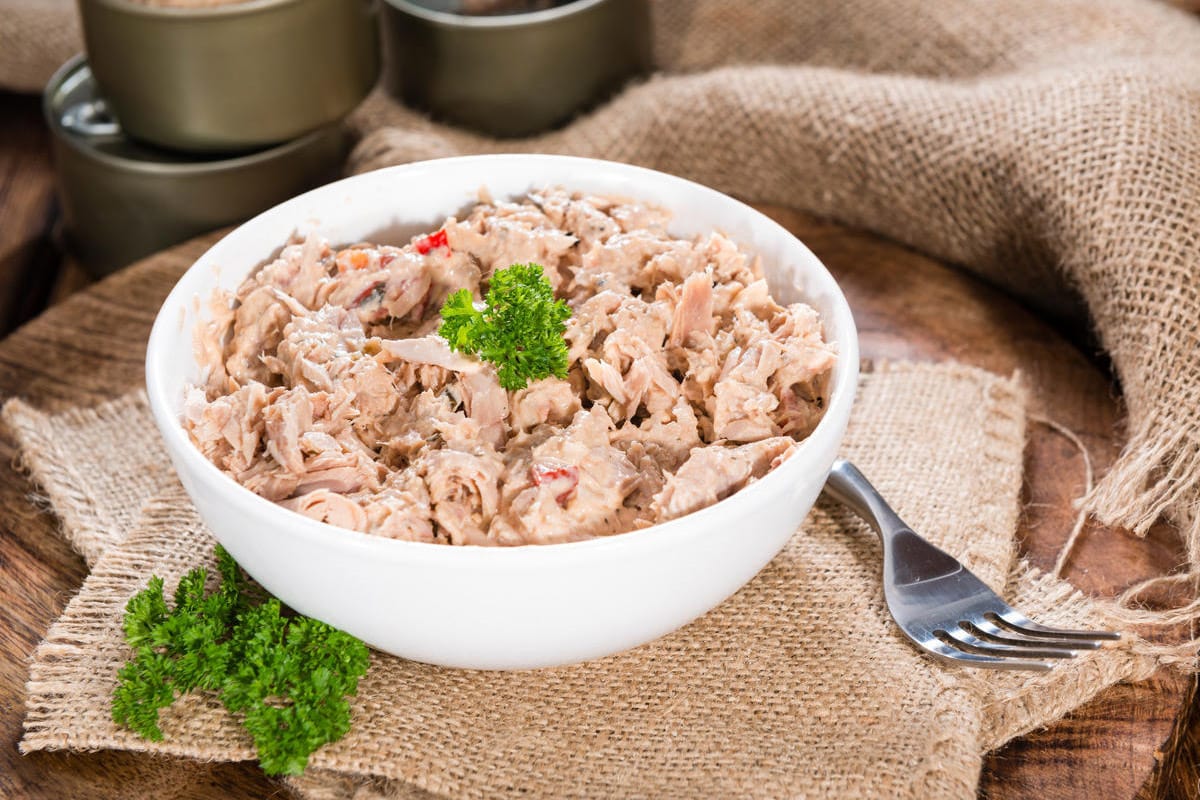 White plate with canned tuna, parsley on a rustic background.